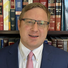 photo of owner standing before books wearing suit.